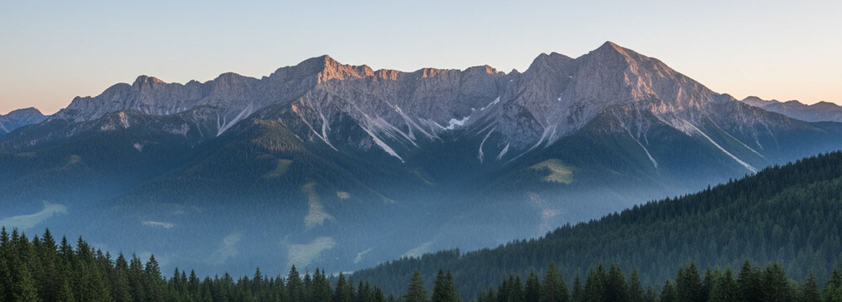 A long gray limestone ridge catching first light above dark spruce forest, with old snow lying in shaded hollows below the summits.