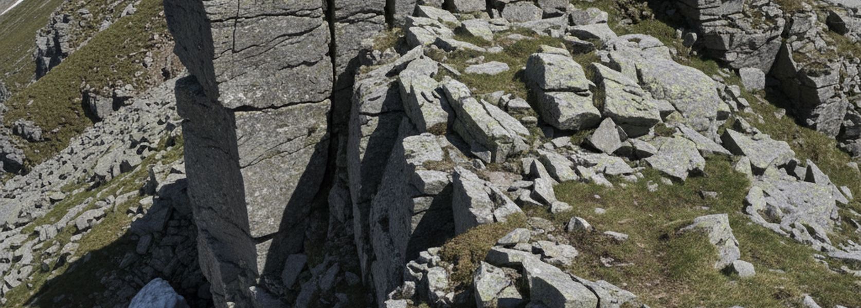 A broken crest of gray granite blocks with lichen and short turf between them, a shaded cleft through the center.